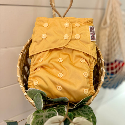 yellow cloth diaper with adjustable snaps in a basket with greenery on the bottom 